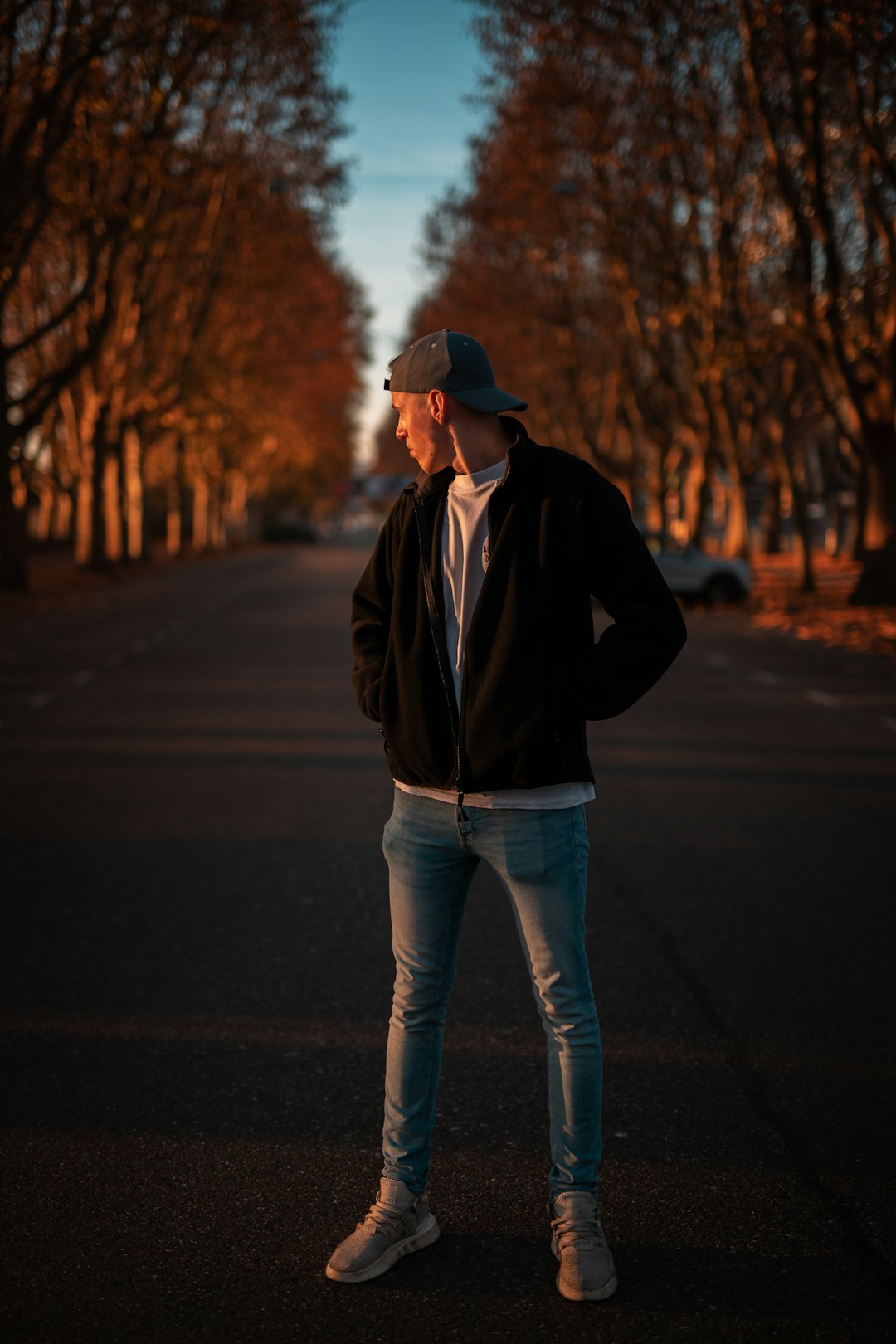 man in black jacket and blue denim jeans standing on road during daytime