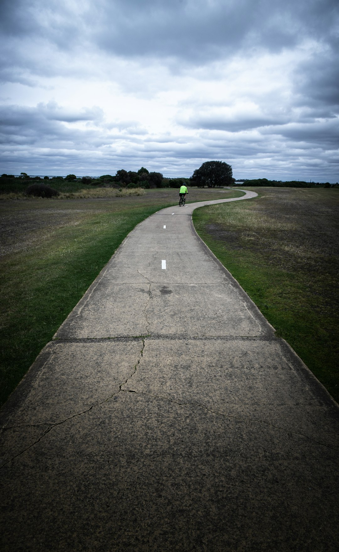 gray concrete road between green grass field under gray clouds during daytime