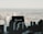 A black rectangular sign with the word 'Renovarde' written on it in white cursive font is placed against a blurred cityscape in the background. The foreground features the silhouette of what appears to be miniature buildings or parts of a city model.