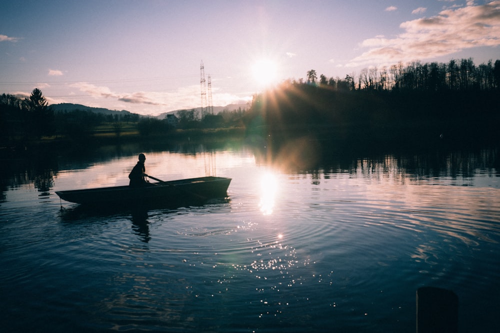 silhouette of person riding canoe on calm water during sunset