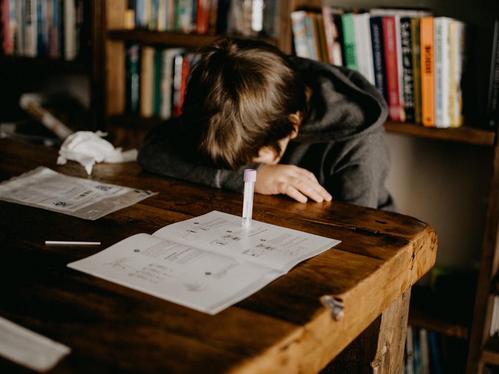 Junge in grauem Kapuzenpulli liest Buch auf braunem Holztisch