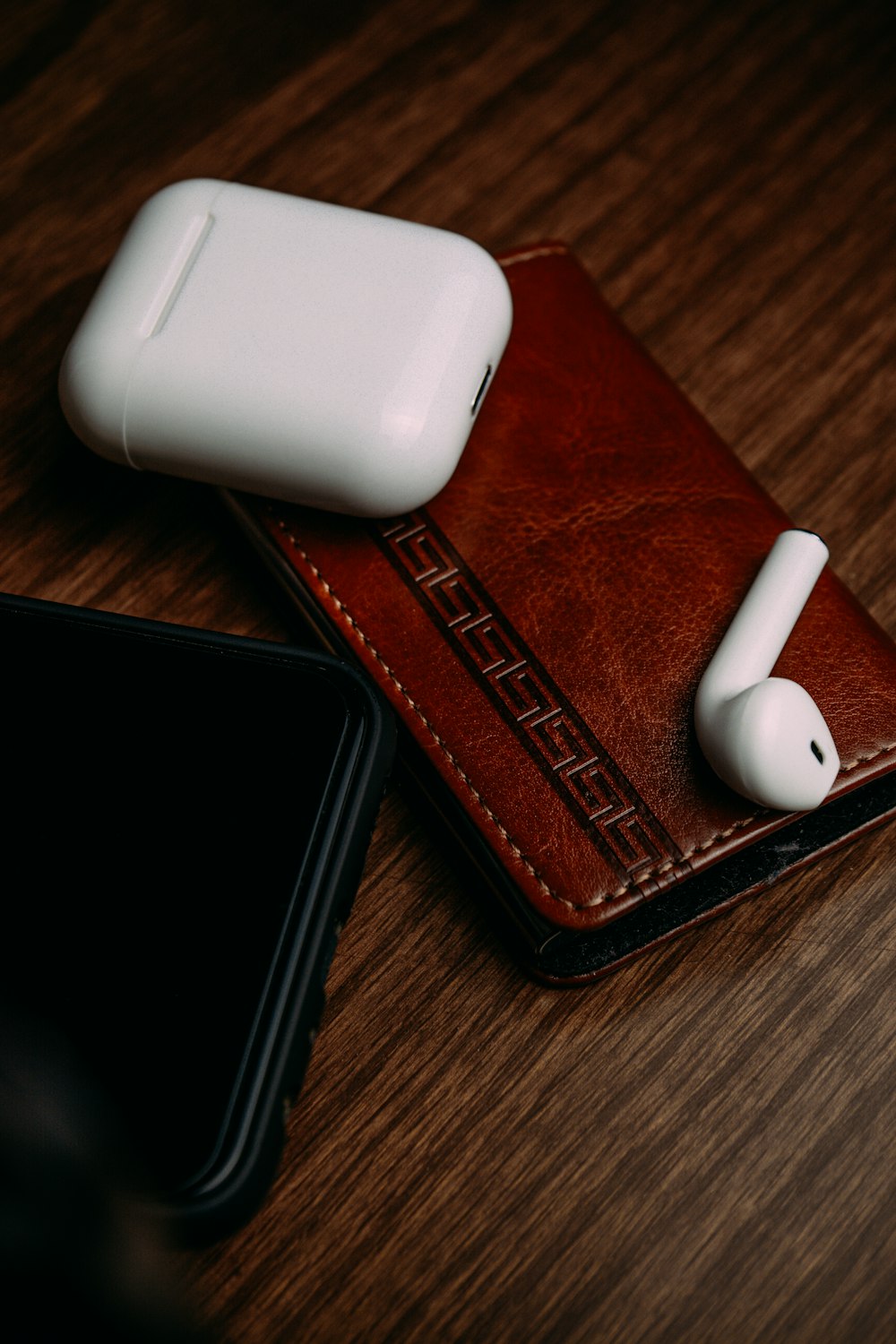 white apple airpods beside brown leather bifold wallet