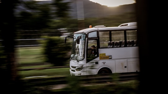 Modern corporate shuttle bus driving on a highway surrounded by green hills.