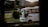 A white bus is captured in motion, driving along a road with a blurred background of greenery and hills. The bus appears to be empty except for the driver, and the light suggests it is either early morning or late afternoon.
