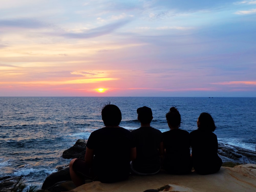 silhouette of people sitting on seashore during sunset