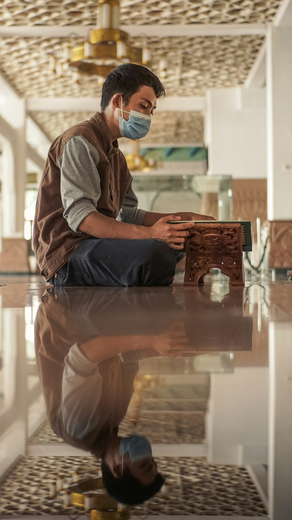 Hombre con sudadera con capucha gris y pantalones azules sentado en una mesa de madera marrón