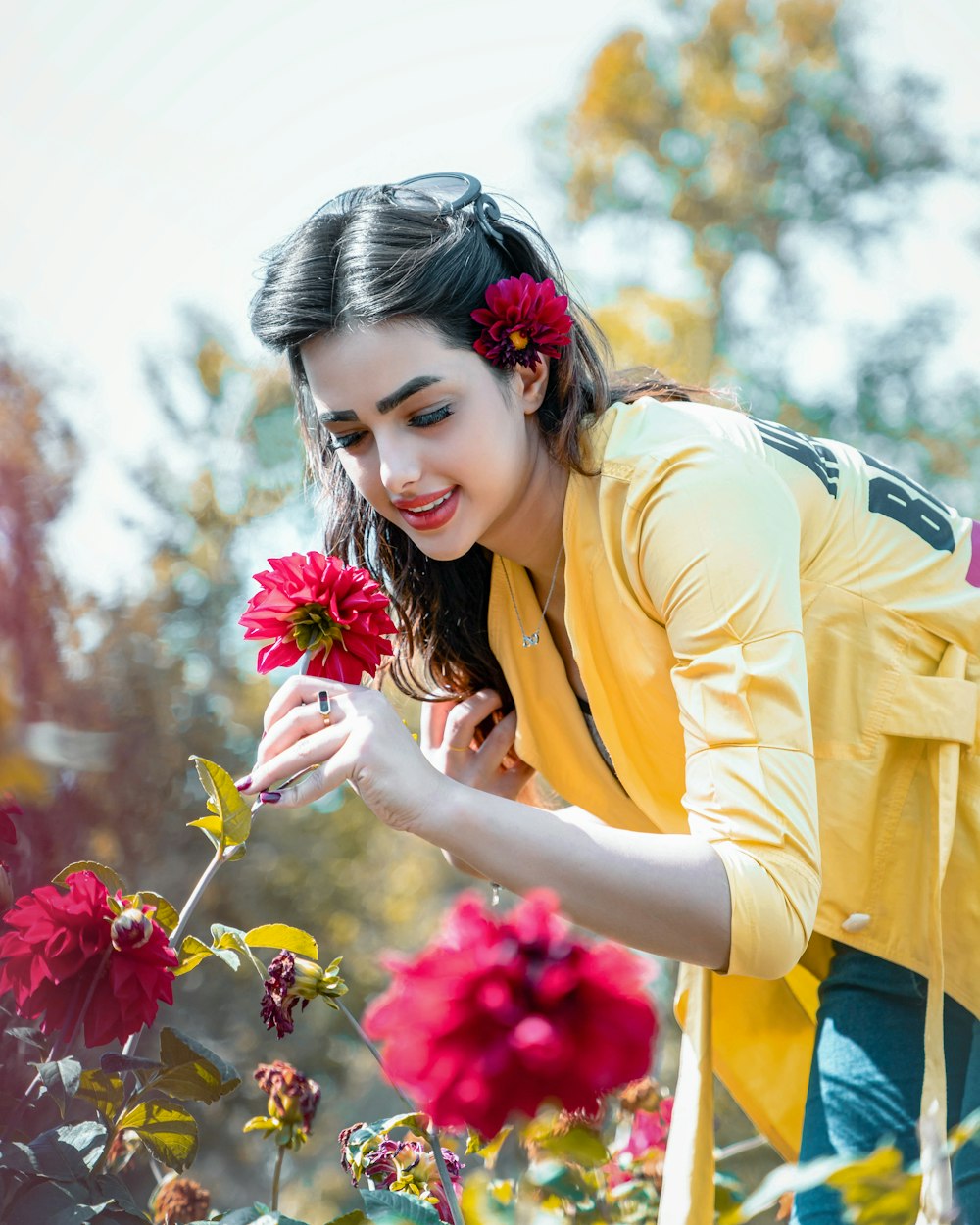 woman in yellow cardigan holding pink flower during daytime