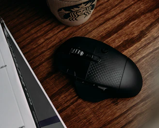 black and gray logitech cordless computer mouse beside white and green starbucks cup