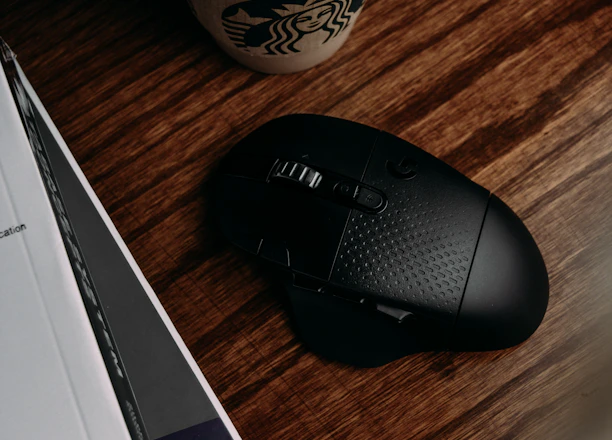 black and gray logitech cordless computer mouse beside white and green starbucks cup