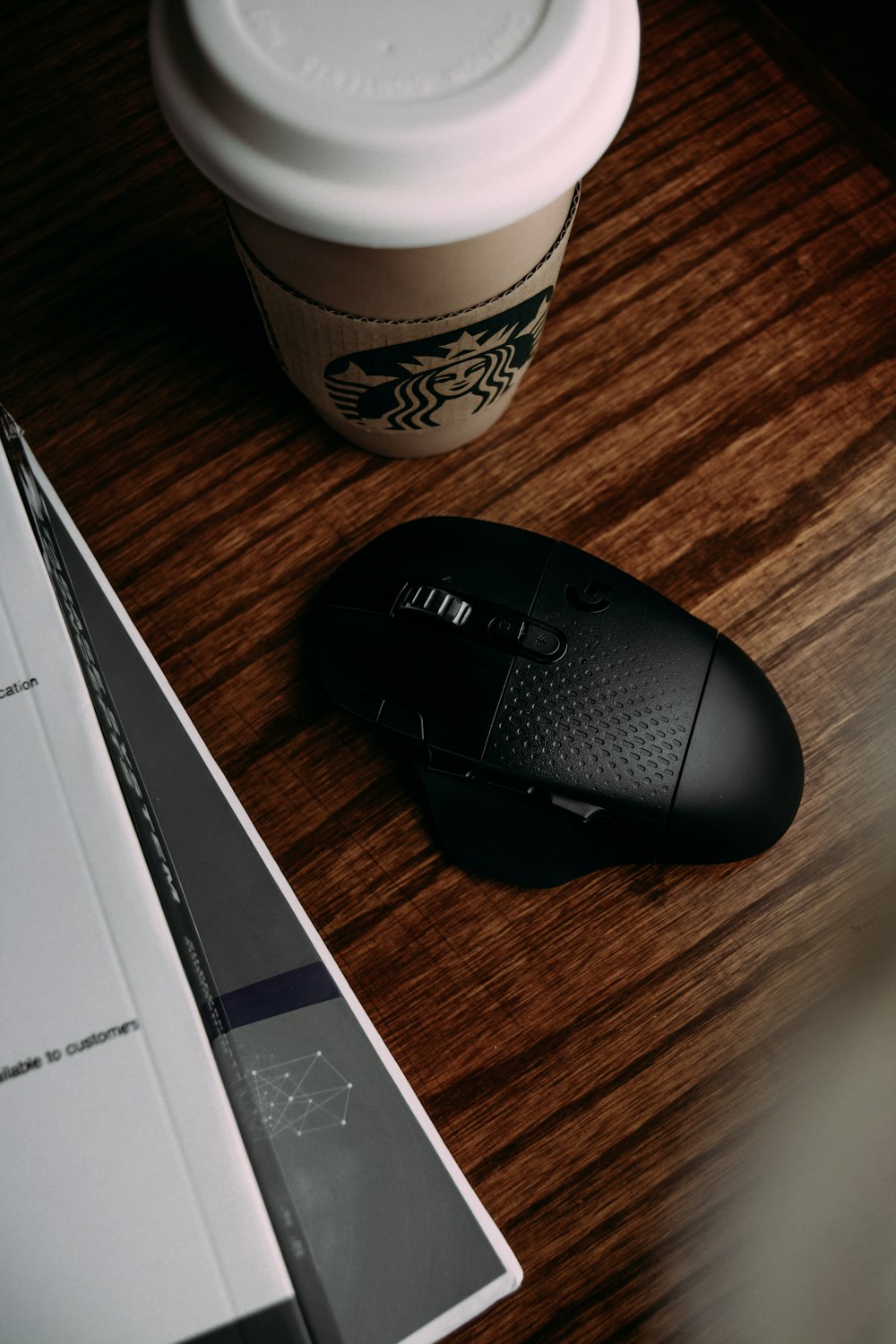 black and gray logitech cordless computer mouse beside white and green starbucks cup
