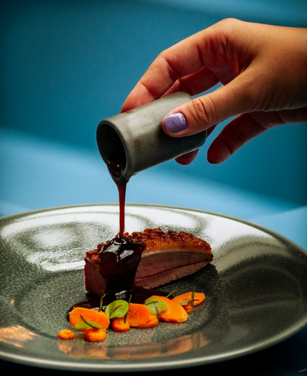 person pouring black liquid on brown chocolate cake