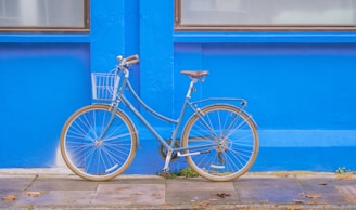 un vélo de ville bleu clair avec un petit panier à l'avant, posé devant un mur bleu