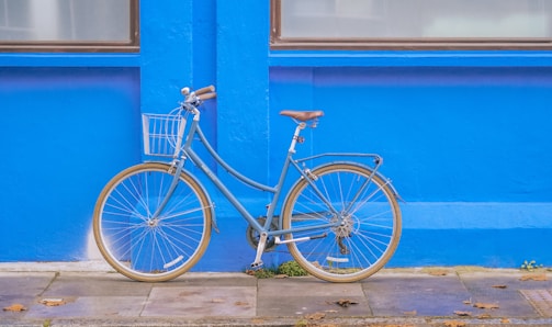 un vélo de ville bleu clair avec un petit panier à l'avant, posé devant un mur bleu