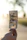 A hand holds a crumpled US hundred-dollar bill against a blurred outdoor background with soft sunlight. The focus is on the bill, while the background appears serene and out of focus.