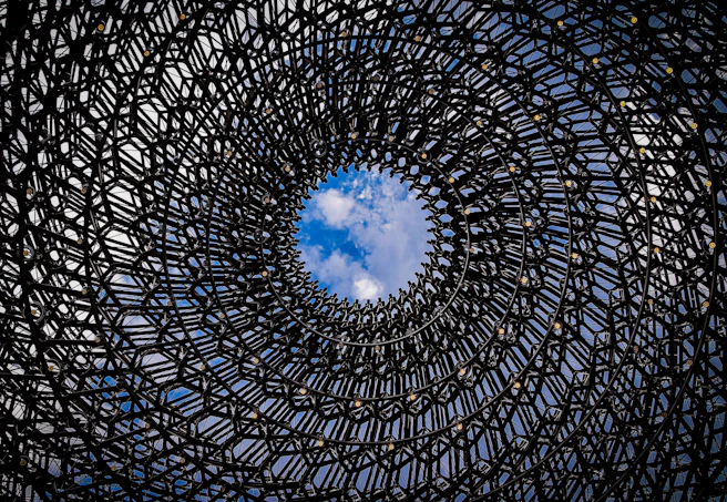fractal dome structure climbs upward with a skylight revealing a bright partly cloudy sky