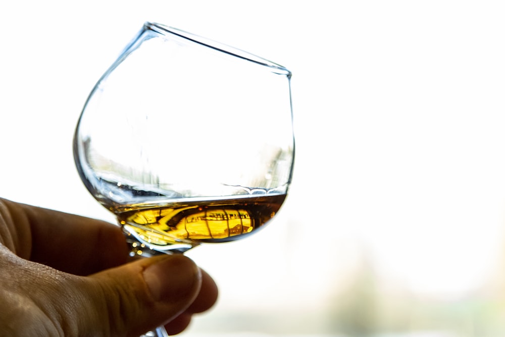 person holding clear wine glass with brown liquid