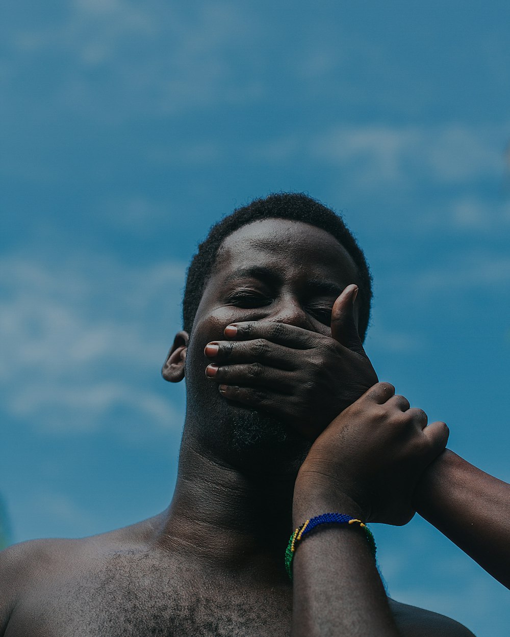 woman in blue and green bracelet covering her face with her hand