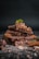 A stack of chocolate pieces, adorned with almonds and a fresh mint leaf on top, scattered with chocolate shavings and nuts around on a dark background.
