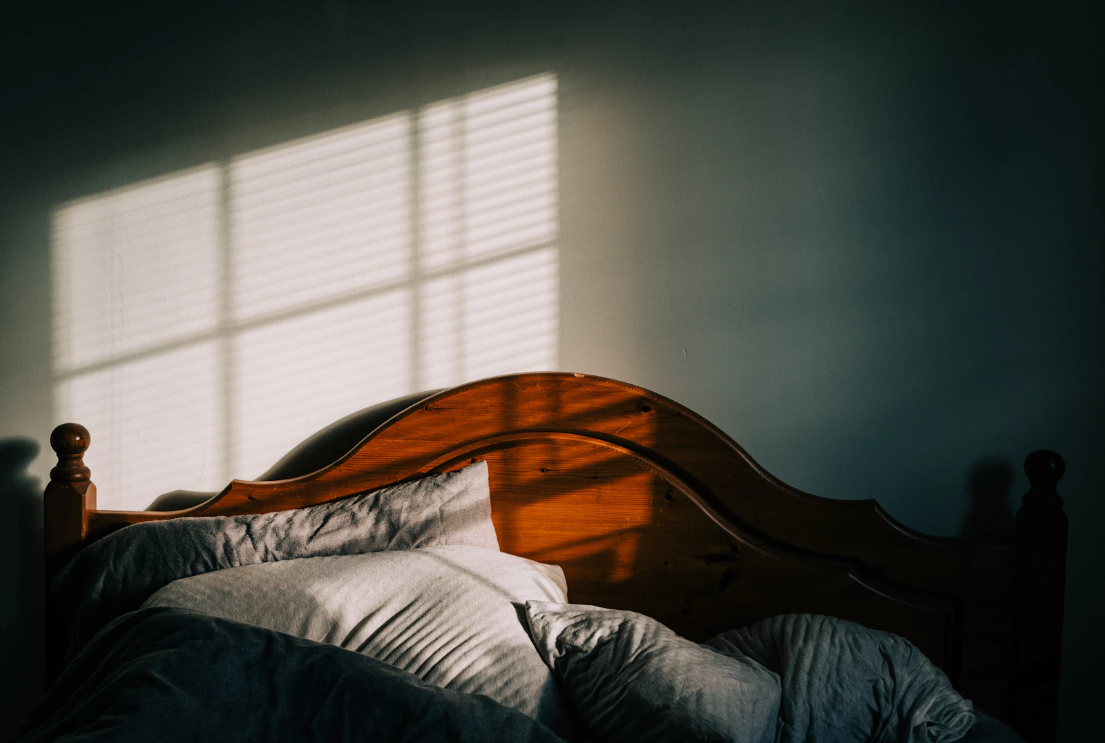 A neatly made bed with a wooden headboard and clean white linen, morning light through the window