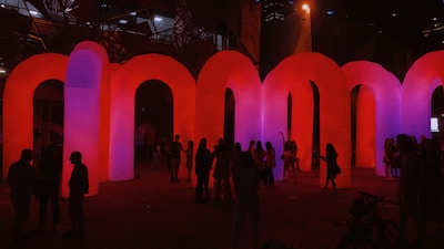 A candid moment of festival attendees engaging in lively conversation near a red-lit art installation.