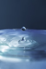 Close-up of a clear water droplet falling into a calm blue pool, reflecting purity.