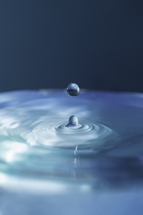 A serene image of clear bottled water with droplets on the surface, set against a soft blue background.