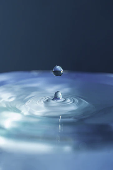 Crystal-clear drop of purified water falling into a serene glass bowl.