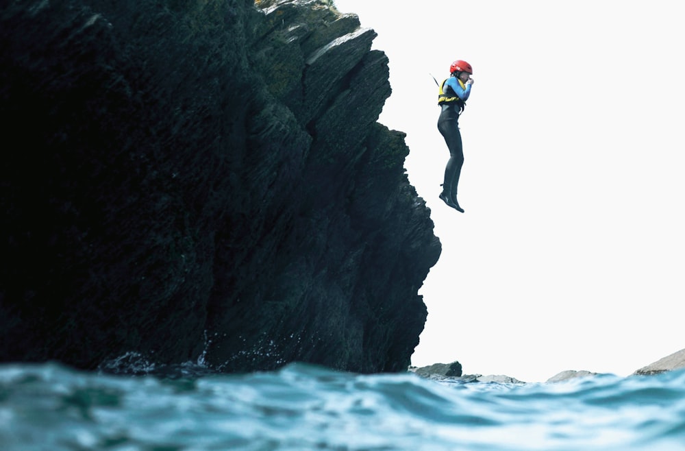 man in green shirt and black pants jumping on rocky mountain during daytime