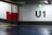 An indoor parking lot with a large U1 sign painted on the wall. The environment features concrete walls with a grey base and a red and white section. A green exit sign with an arrow points left, and the floor is coated with a blue finish. There is a pedestrian control sign on the red section of the wall.