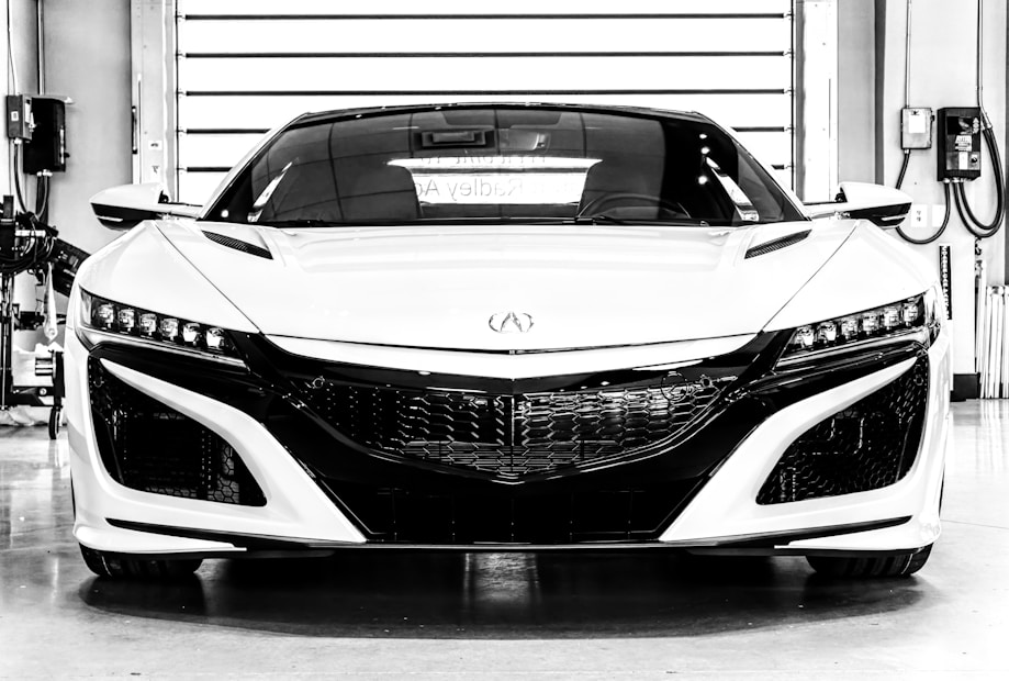 A sleek, modern sports car is positioned inside a garage with various equipment visible in the background. The car has a glossy finish, sharp lines, and prominent headlights, showcasing a sense of power and sophistication.