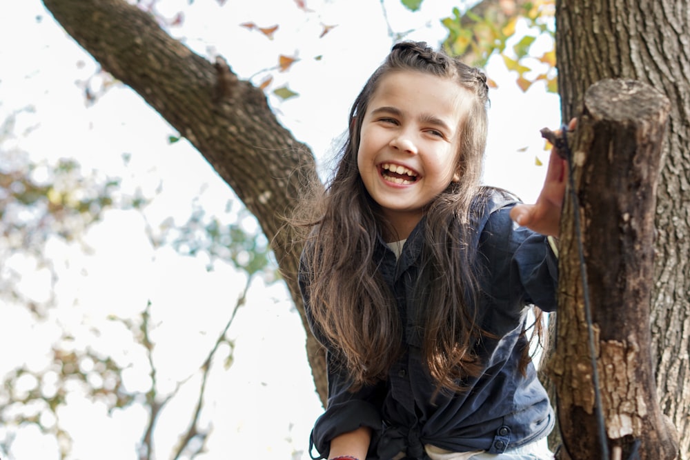 woman in black leather jacket standing beside brown tree during daytime