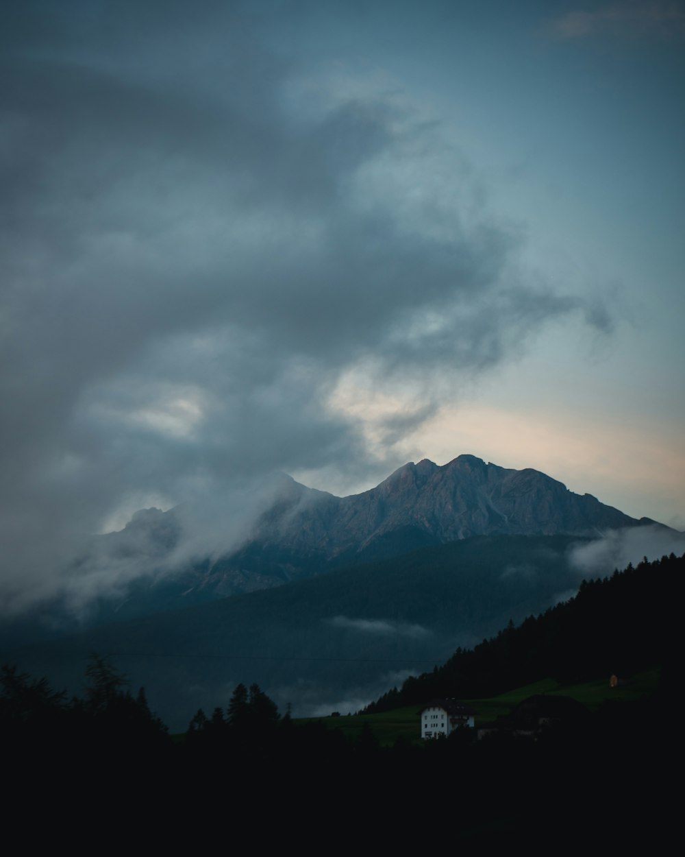 green grass field near mountain under white clouds during daytime