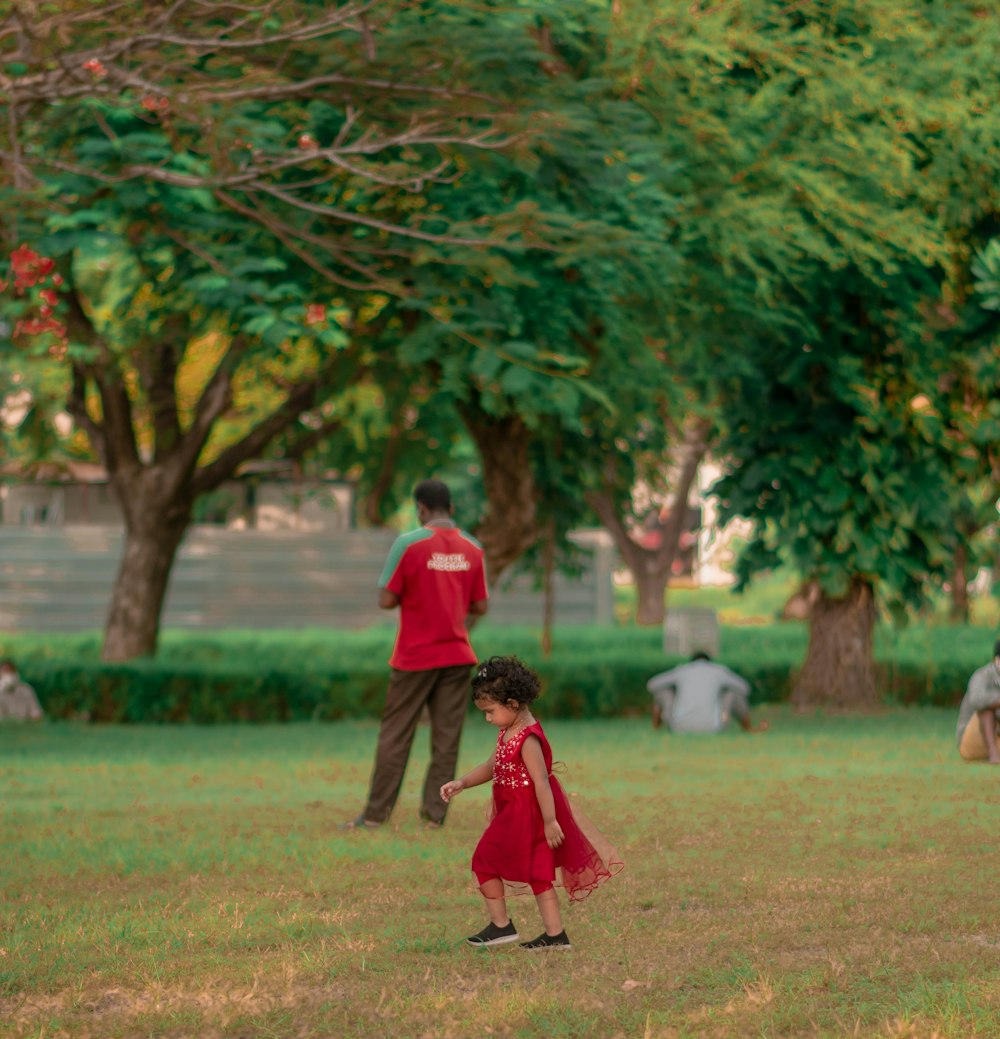 boy in red shirt walking on green grass field during daytime