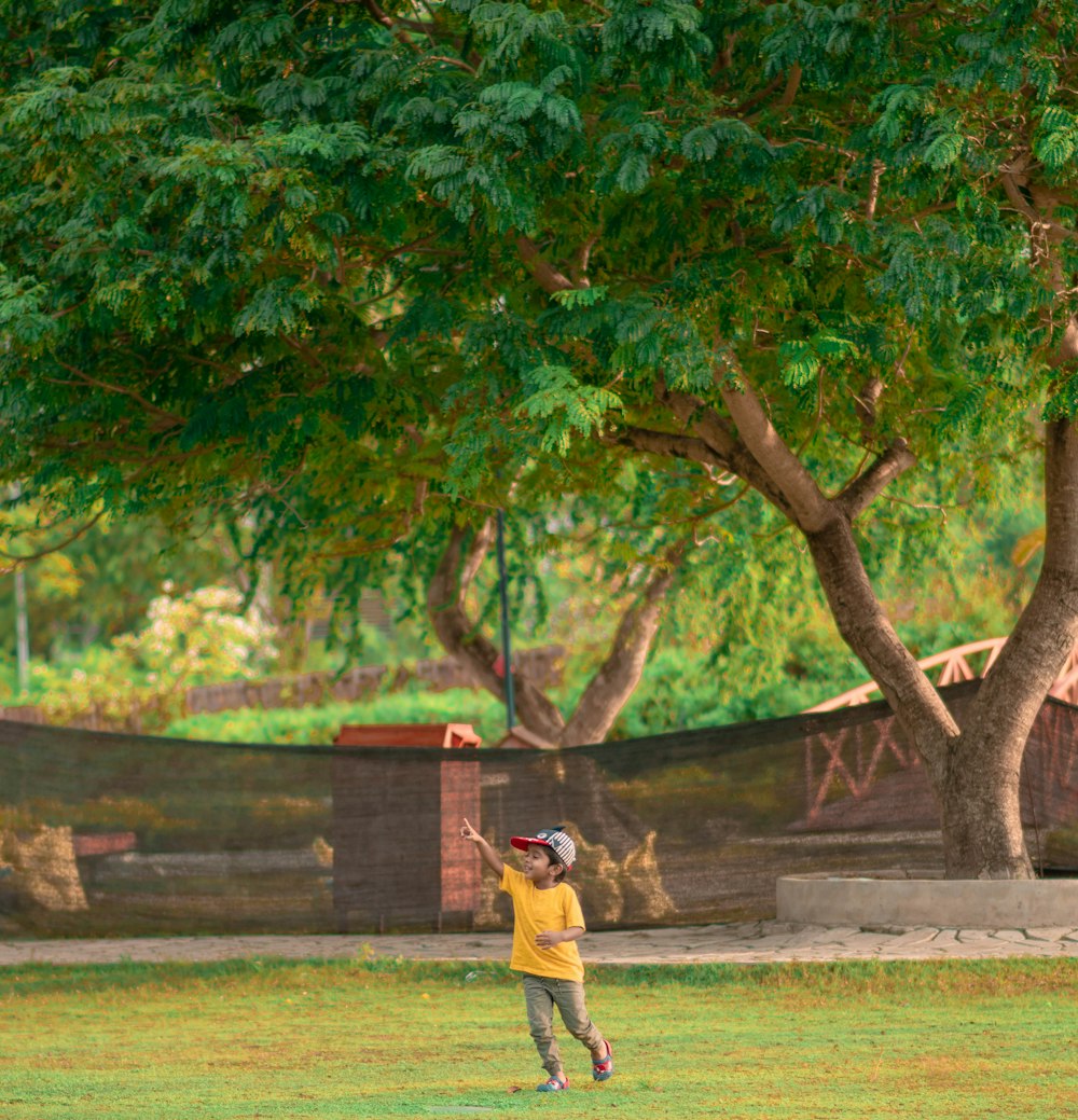 boy in yellow shirt and brown shorts standing on green grass field during daytime
