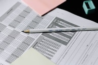 A standardized test answer sheet with multiple-choice bubbles is accompanied by a pencil and a pencil sharpener. Overlapping sheets with filled and unfilled circles indicate test preparation or completion. Colored sticky notes are placed nearby, suggesting organization or note-taking.