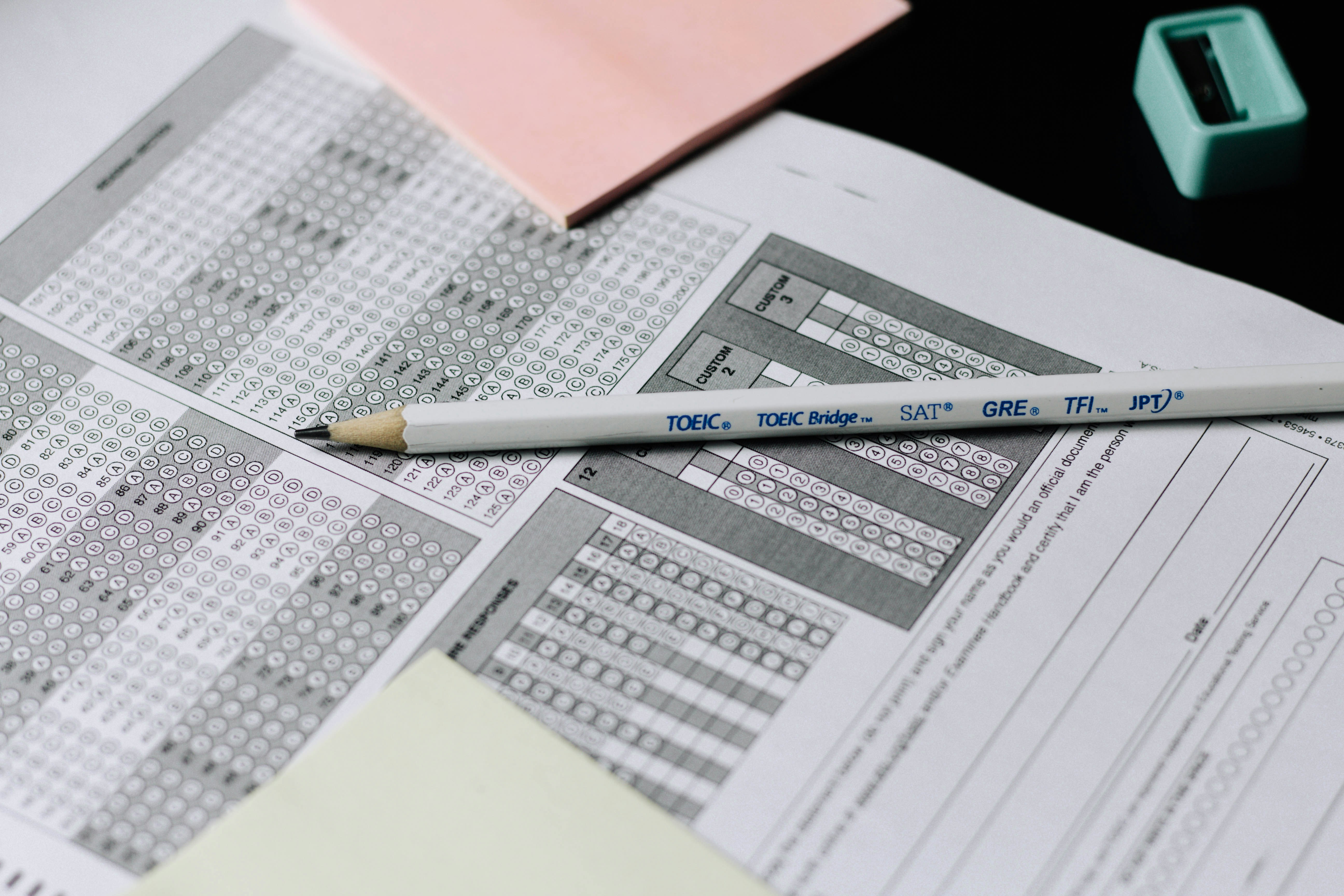 A pencil resting on a multiple choice answer sheet with pink sticky notes