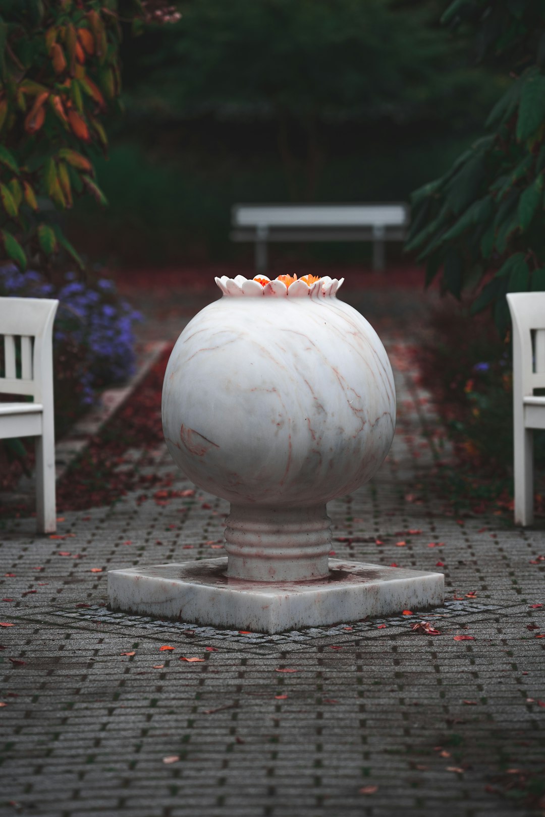 white ceramic round vase with orange flowers on gray concrete brick floor