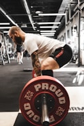 man in white t-shirt and black shorts carrying red and black barbell