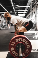 man in white t-shirt and black shorts carrying red and black barbell