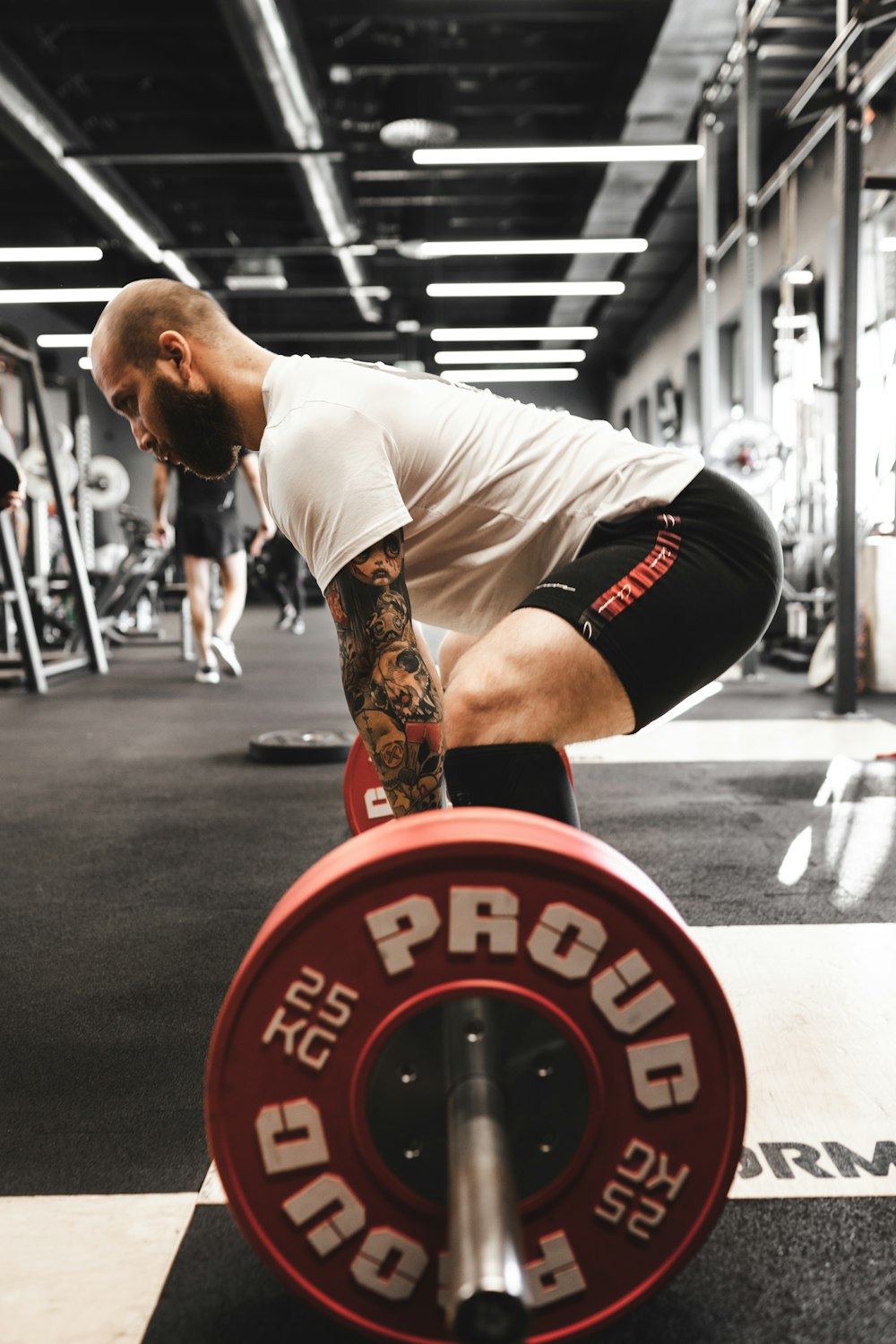 man in white t-shirt and black shorts carrying red and black barbell