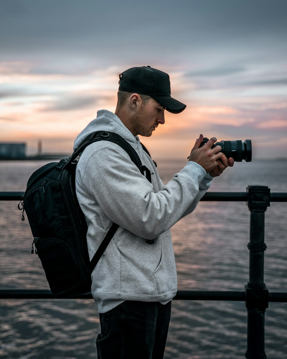 man in gray hoodie and black cap holding black dslr camera