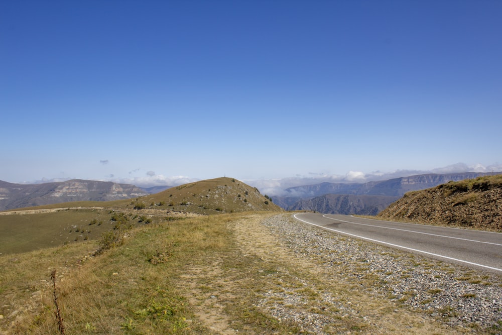 Carretera de asfalto gris cerca de montañas marrones bajo cielo azul durante el día