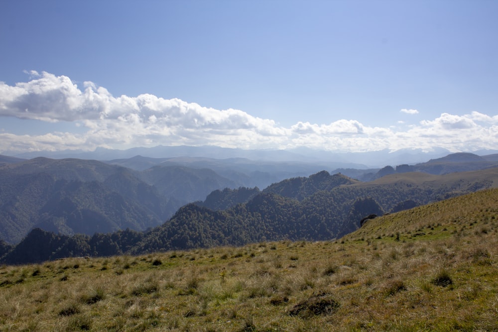 green grass field and mountains under white clouds and blue sky during daytime