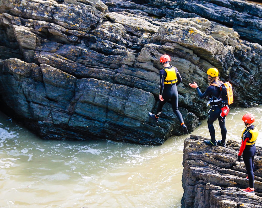 3 men and woman in yellow and black wet suit standing on rocky shore during daytime