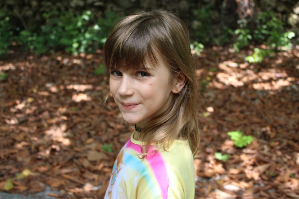 girl in yellow and pink shirt standing on brown leaves during daytime