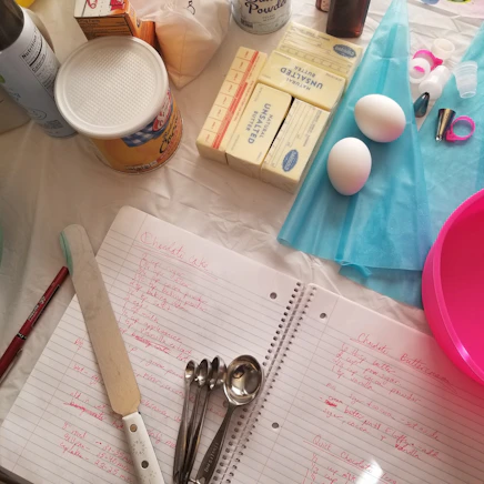 Assorted cake decorating kits including spatulas, scrapers, and brushes laid out on a pastel background.