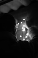 A person is adjusting a string of small lights, possibly decorating or arranging them. The scene is dimly lit, with soft illumination from the lights creating a cozy atmosphere.