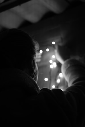 A person is adjusting a string of small lights, possibly decorating or arranging them. The scene is dimly lit, with soft illumination from the lights creating a cozy atmosphere.