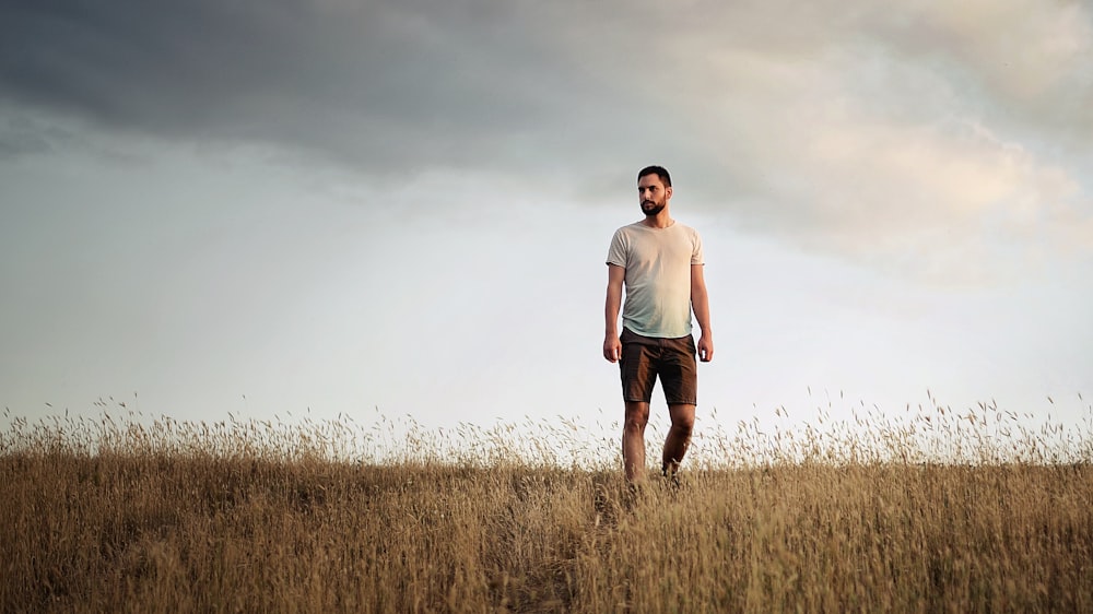 man in white crew neck t-shirt standing on brown grass field during daytime