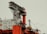 An industrial offshore oil platform featuring large, red structural components and intricate metal frameworks. The platform includes cranes, staircases, and multiple levels, with a beige-painted building section displaying numerous windows.